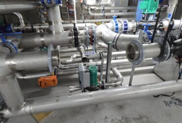 Mechanical contractor installing dense industrial piping system in confined technical space with stainless steel pipes and complex routing